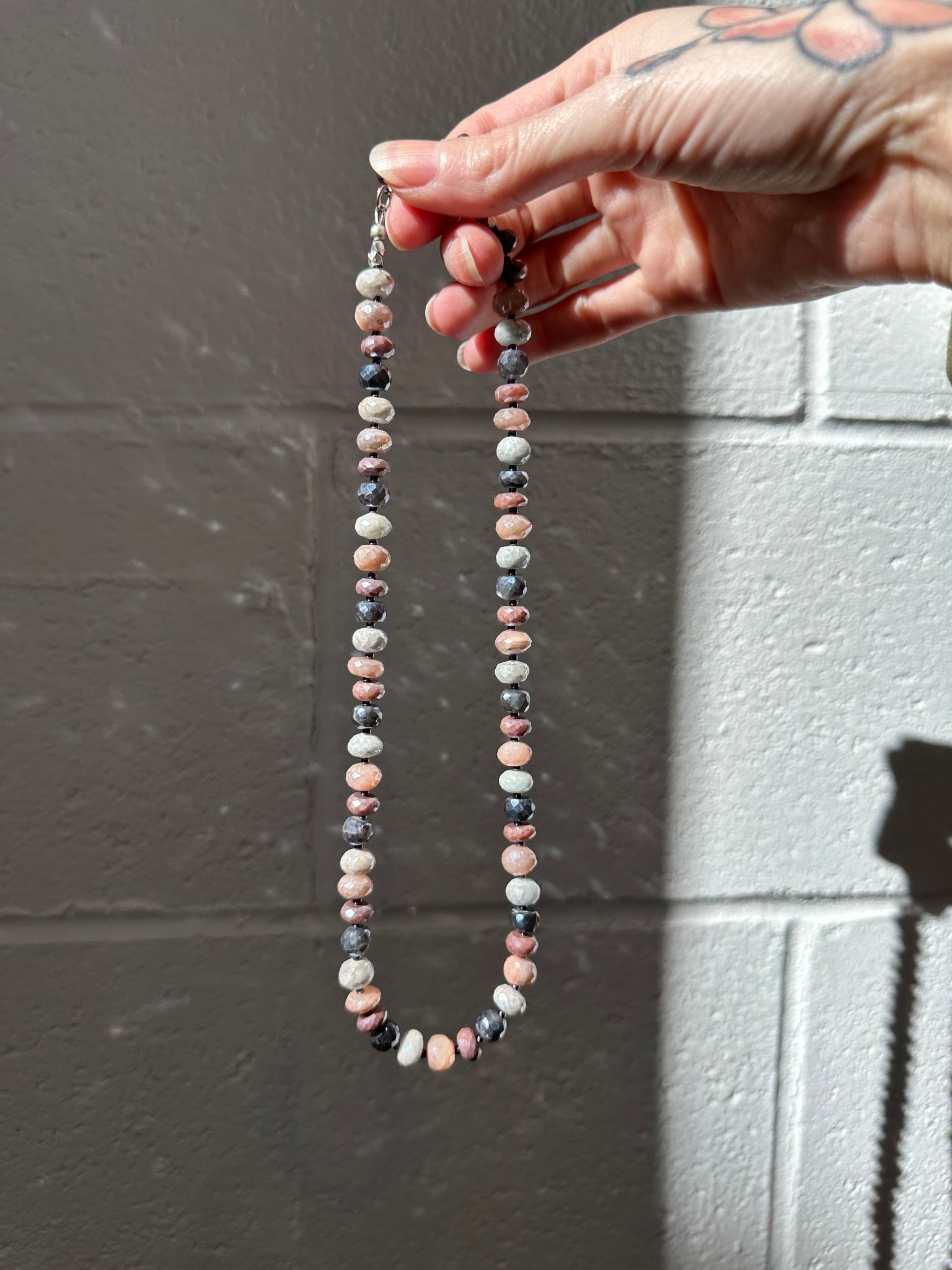 Hand holding a string of small, multicolored beads against a gray background