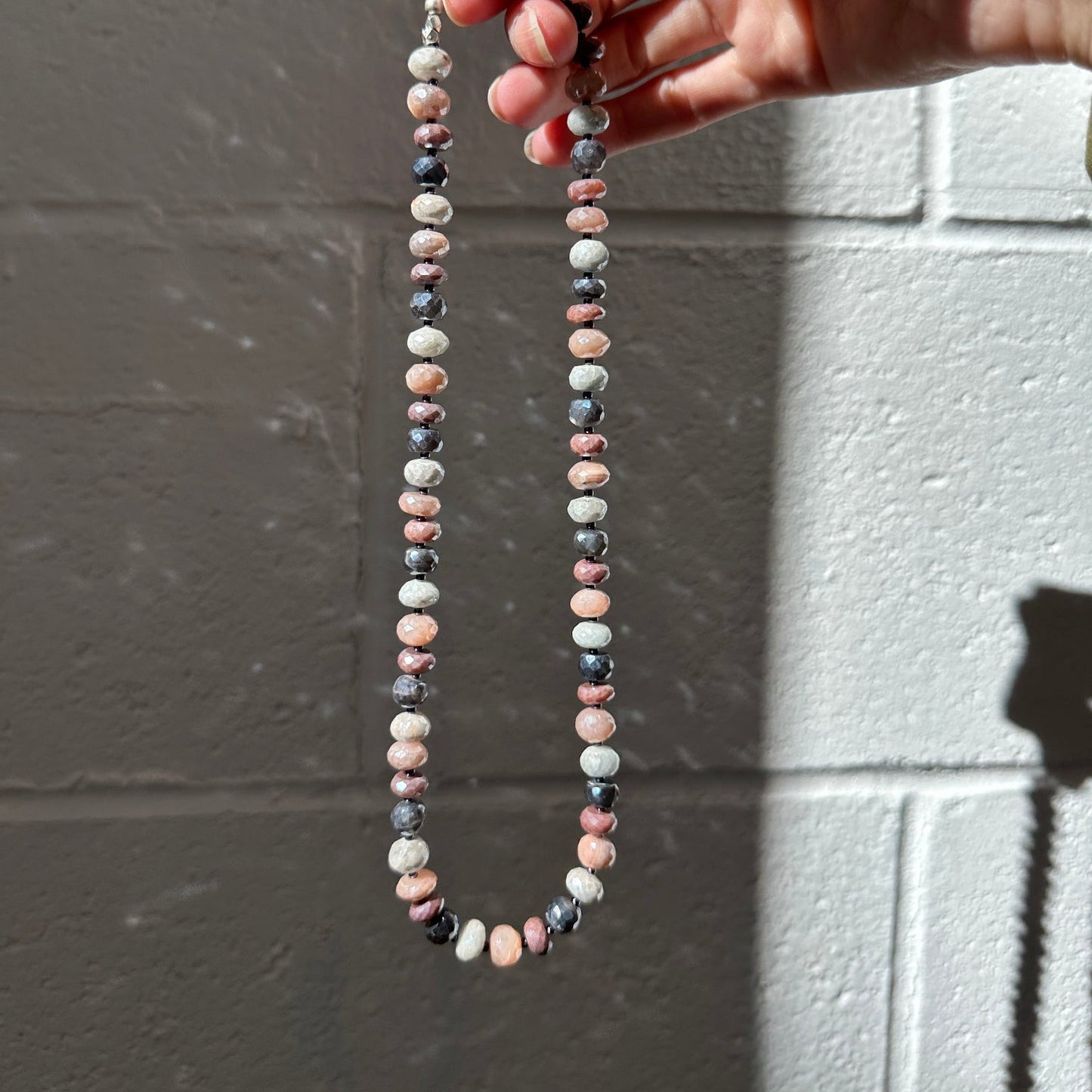 Hand holding a string of small, multicolored beads against a gray background
