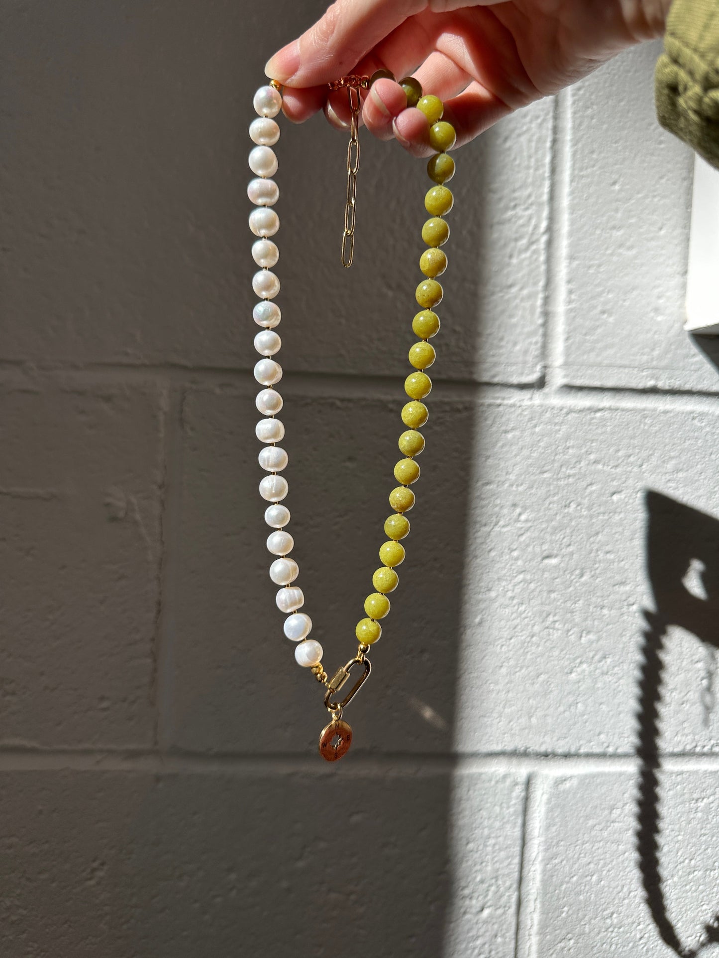 Necklace with green and white beads held by a hand against a tiled wall.