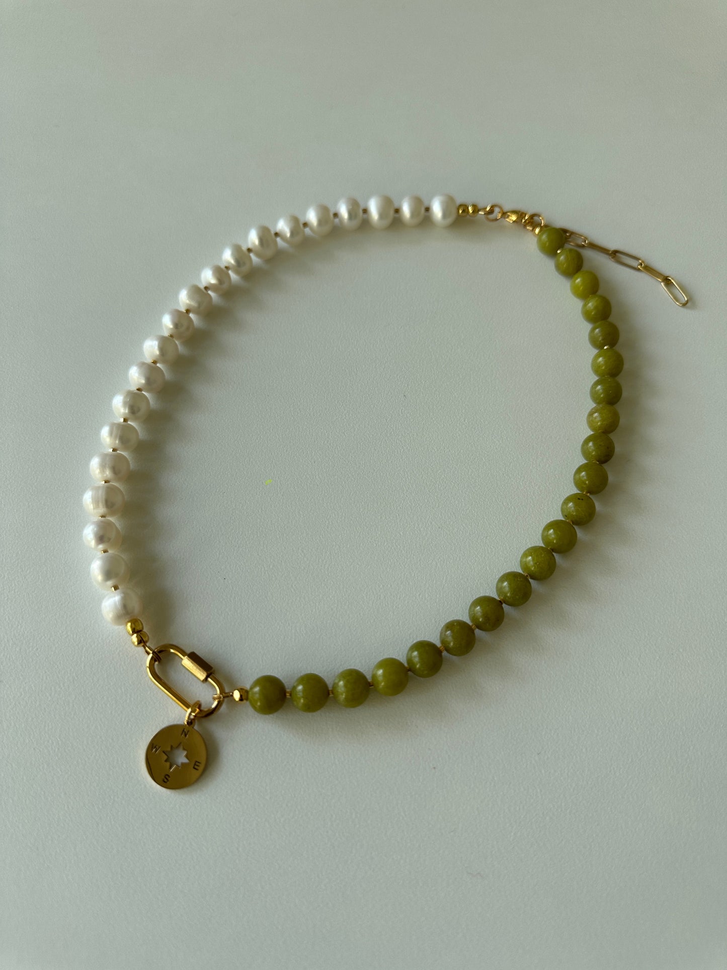 Beaded necklace with jade and pearls and a gold clasp on a light gray background