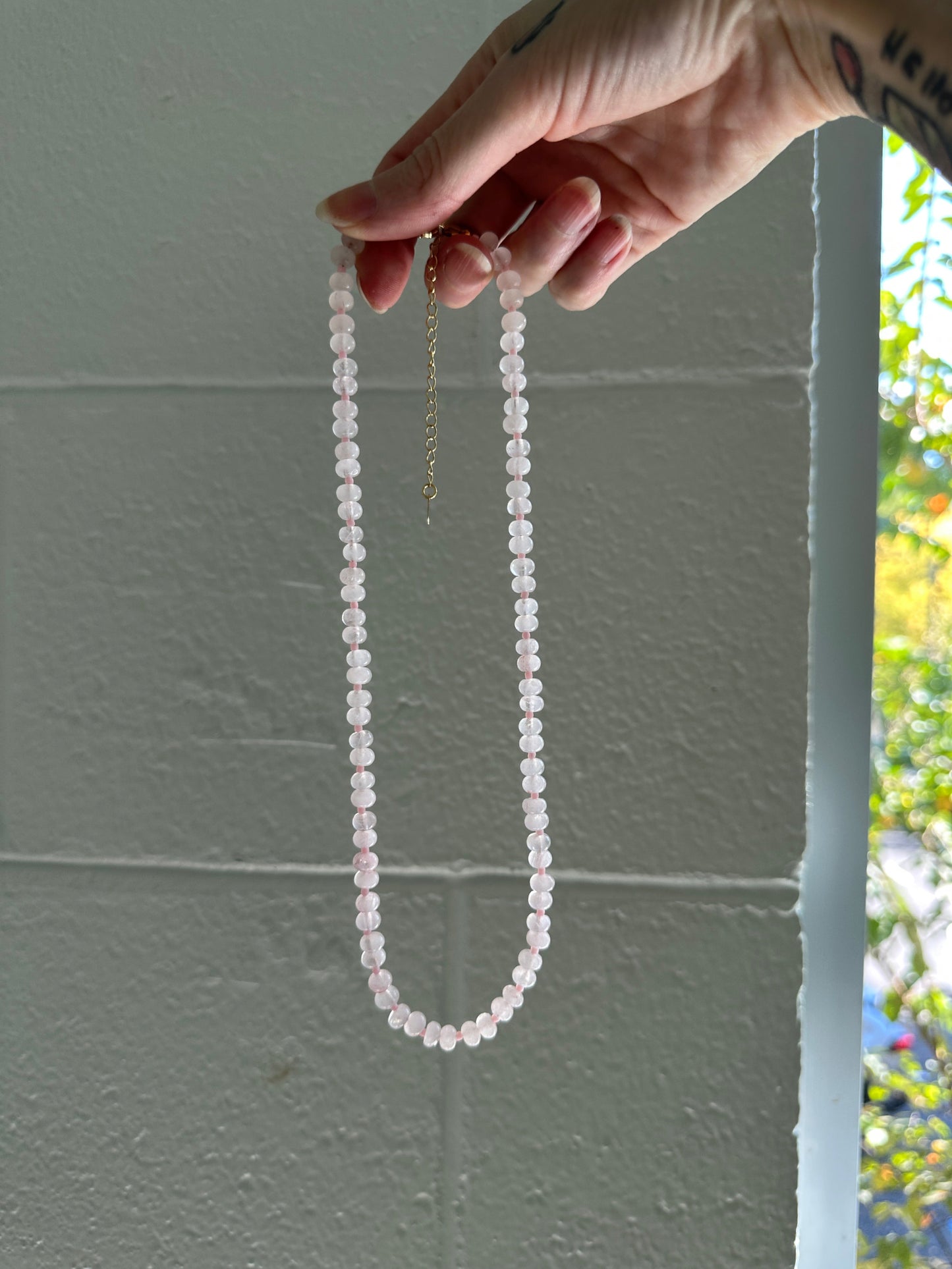 Hand holding a string of rose quartz beads against a light gray wall.