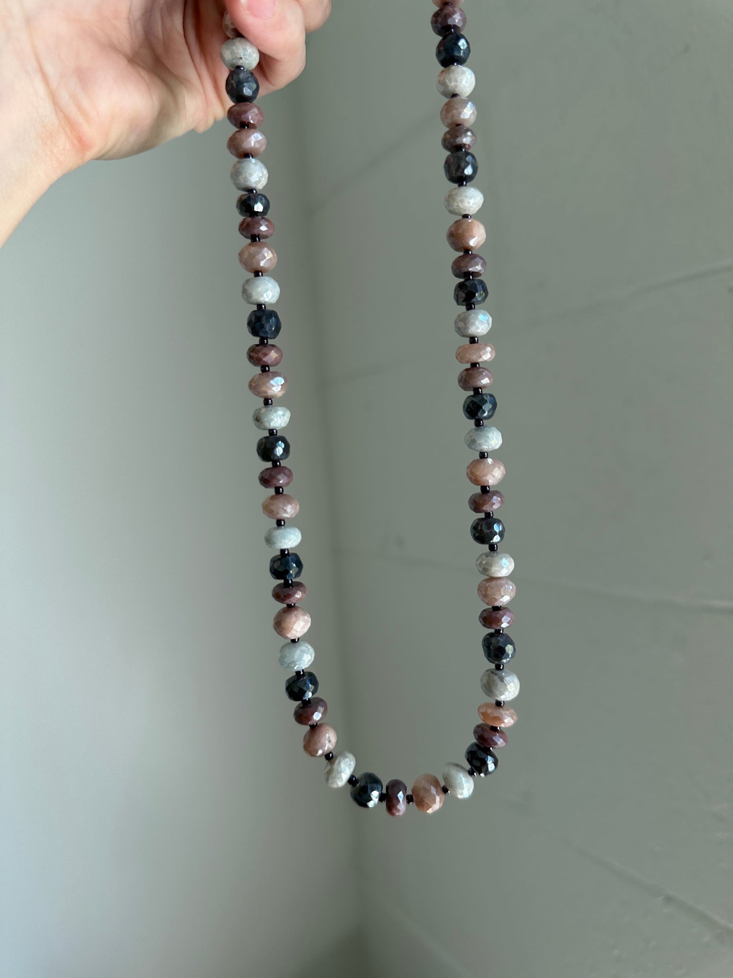 Beaded necklace held by a hand against a plain background