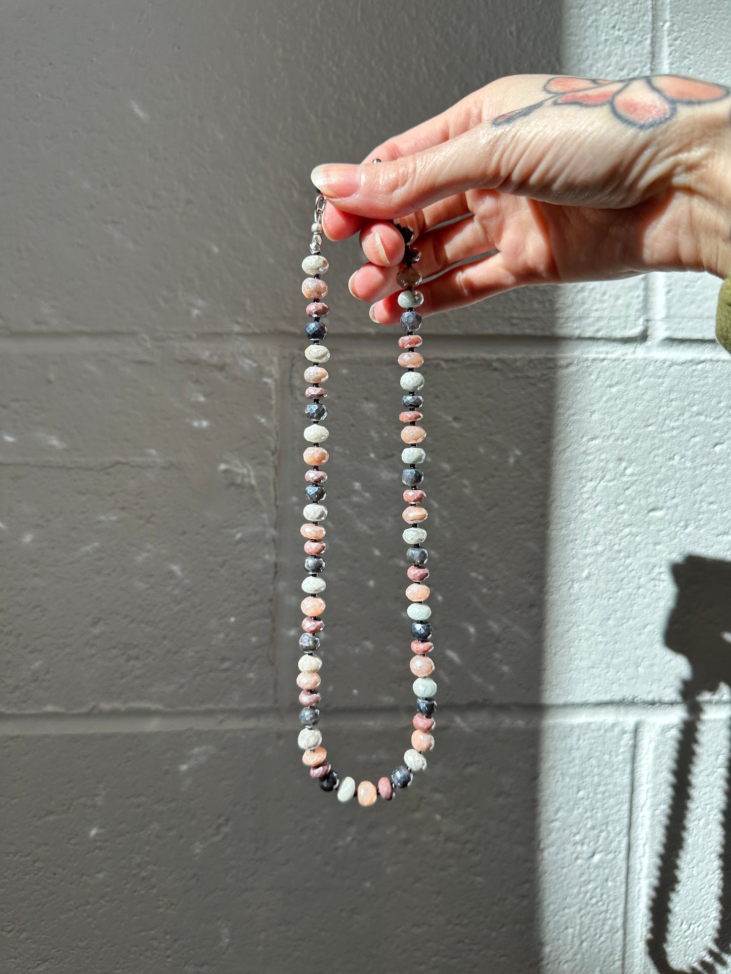 Hand holding a beaded necklace against a gray wall