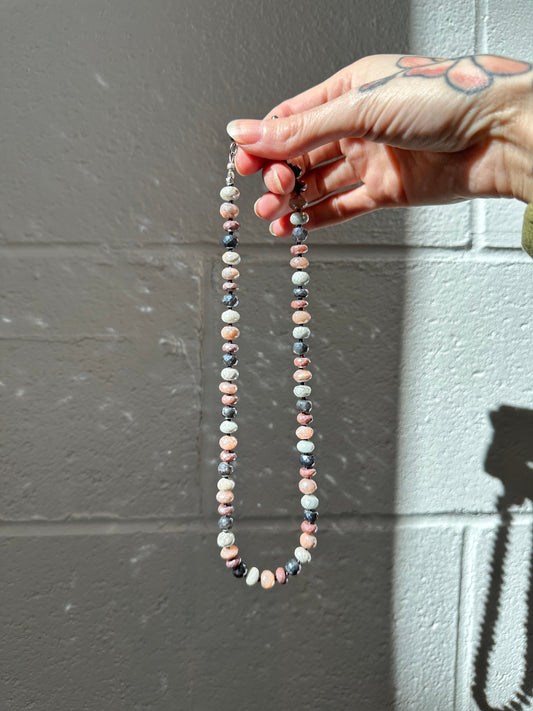 Hand holding a beaded necklace against a gray wall