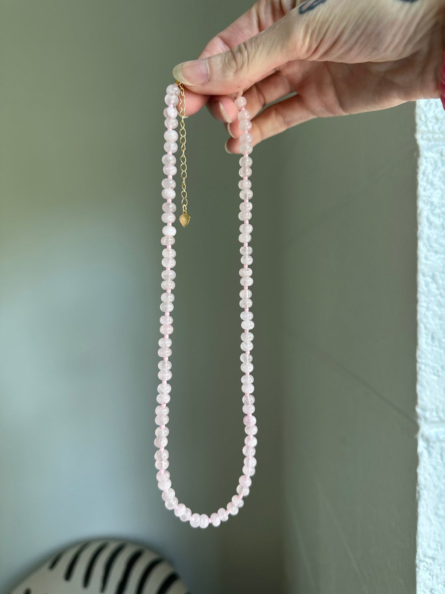 Hand holding a string of rose quartz against a neutral background