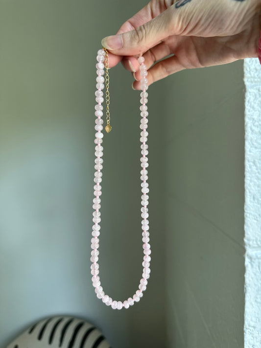 Hand holding a string of rose quartz against a neutral background