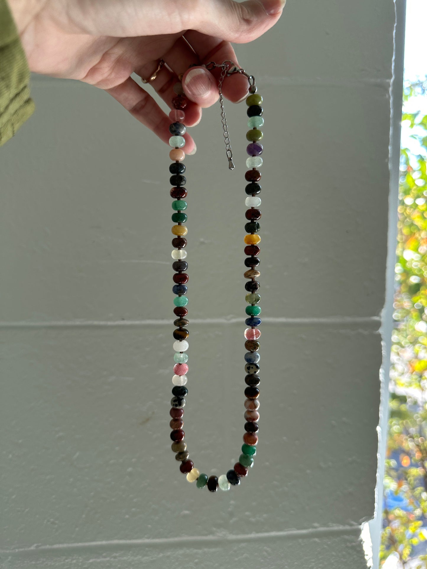 Multicolored beaded necklace held by a hand against a plain background