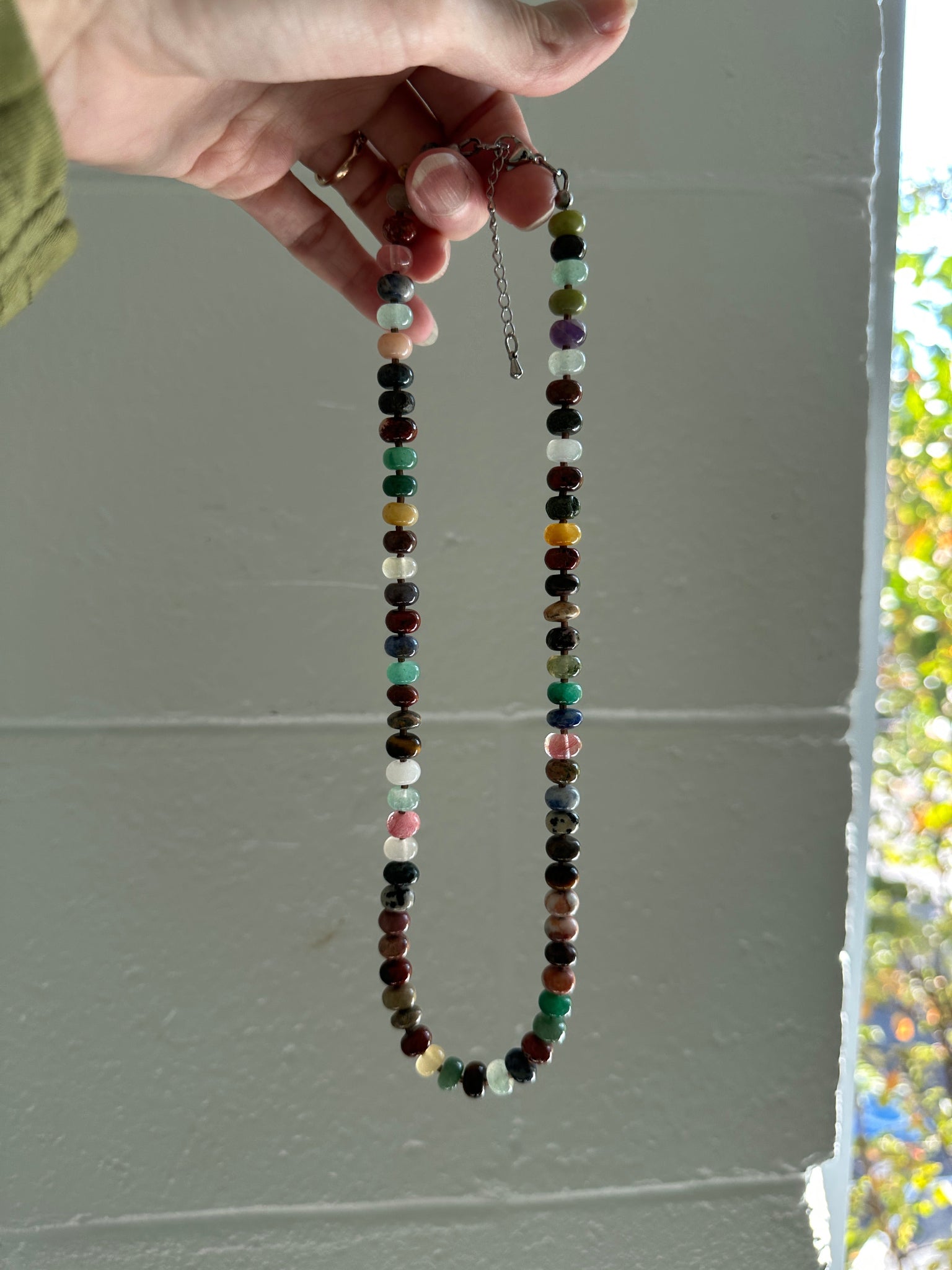 Multicolored beaded necklace held by a hand against a plain background
