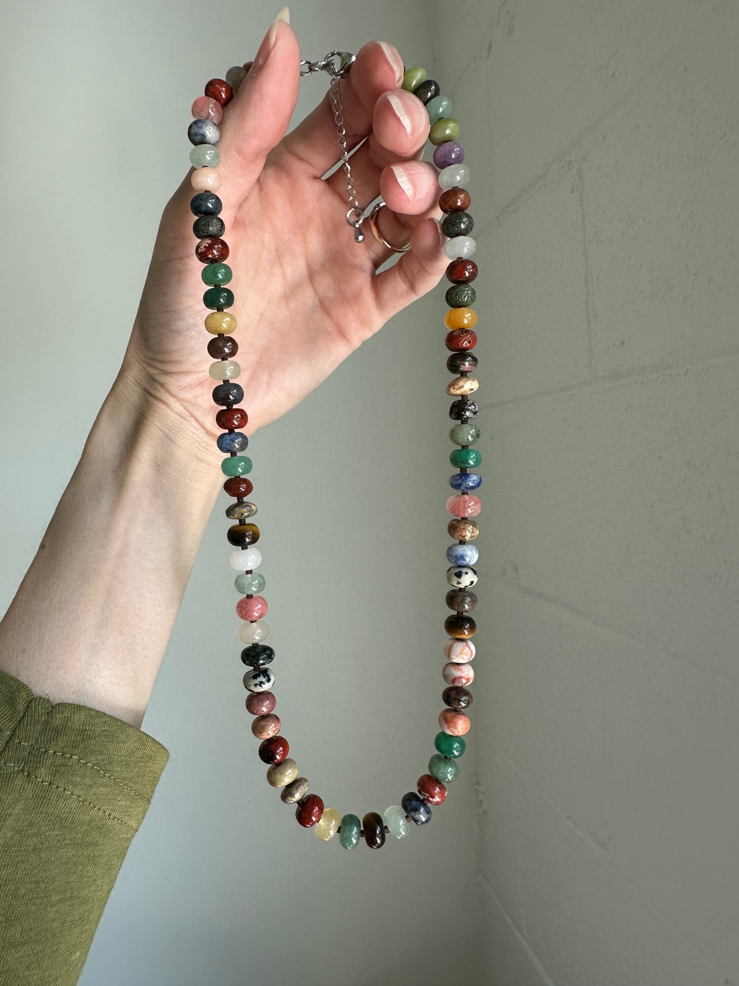 Hand holding a multicolored beaded necklace against a plain background