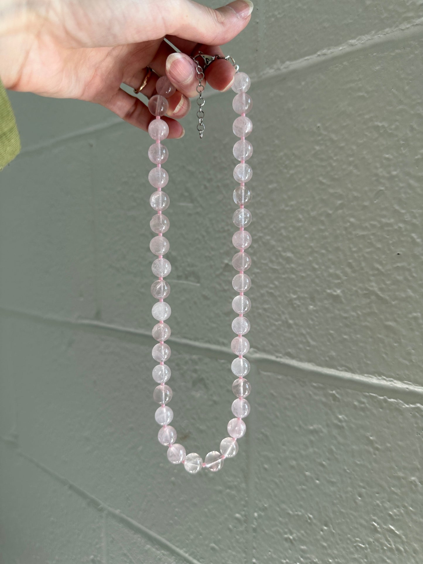 Hand holding a clear beaded necklace against a gray wall