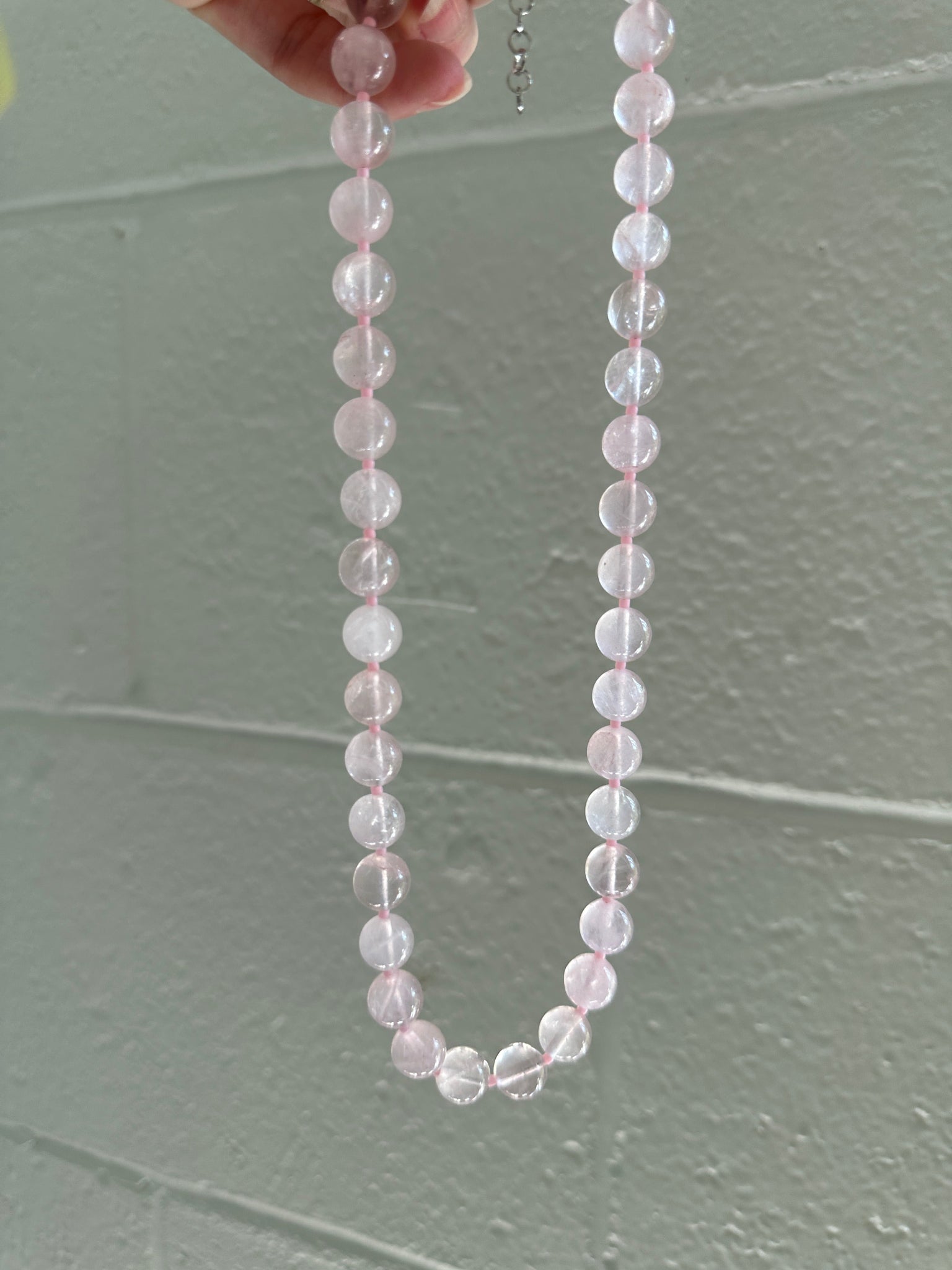 Necklace with clear beads held against a gray tiled wall