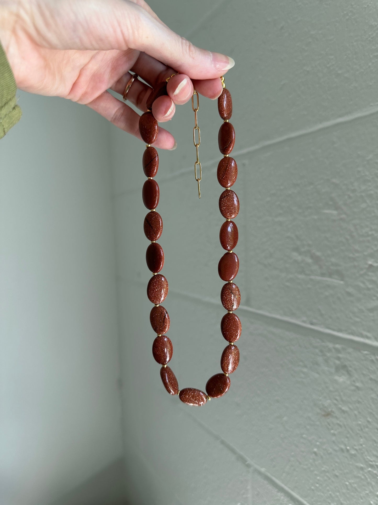 Hand holding  beaded necklace with brown oval beads against a plain background