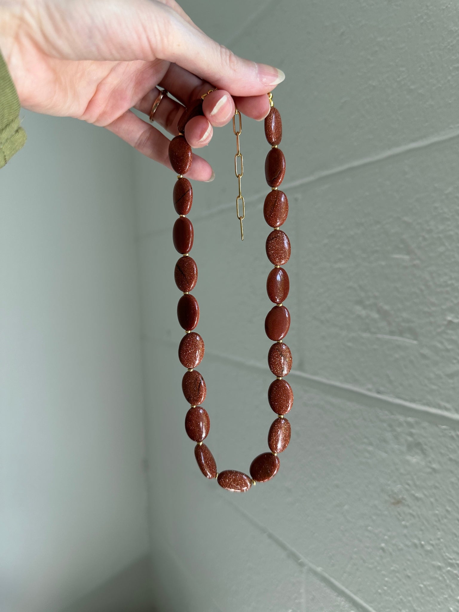Hand holding  beaded necklace with brown oval beads against a plain background