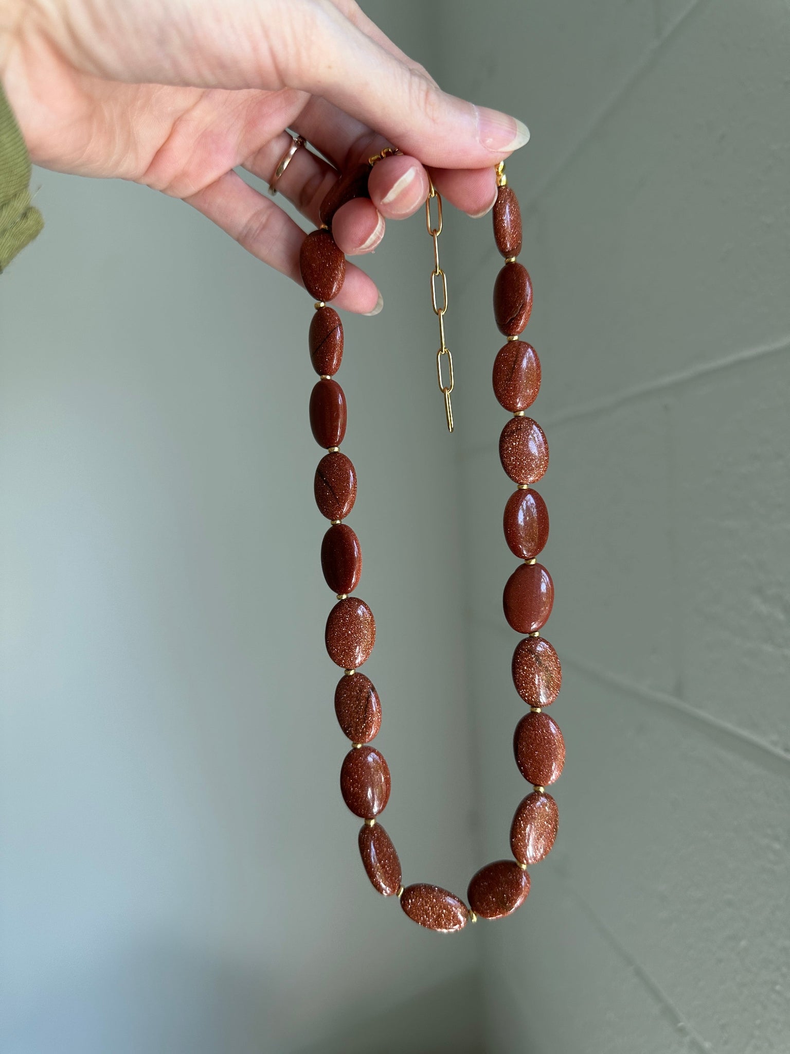 Brown beaded necklace held by a hand against a plain background
