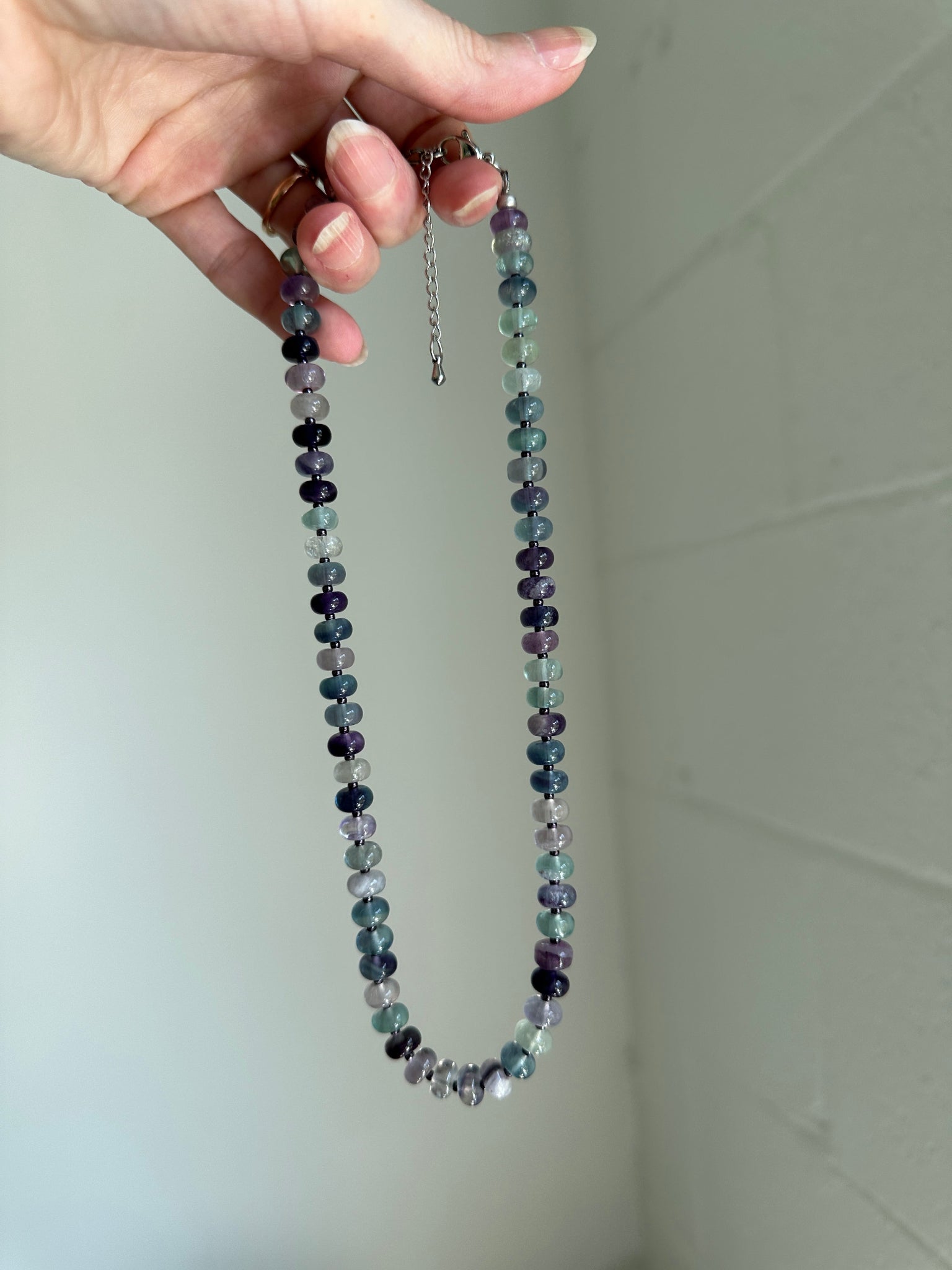 Hand holding a beaded necklace against a plain background