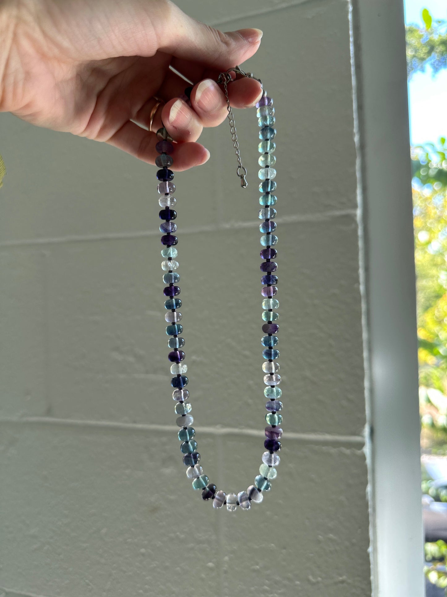 Multicolored beaded necklace held by a hand against a white wall.