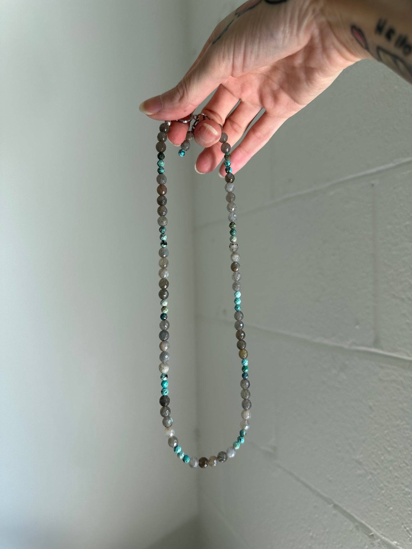 Hand holding a beaded necklace against a white ceiling and wall.