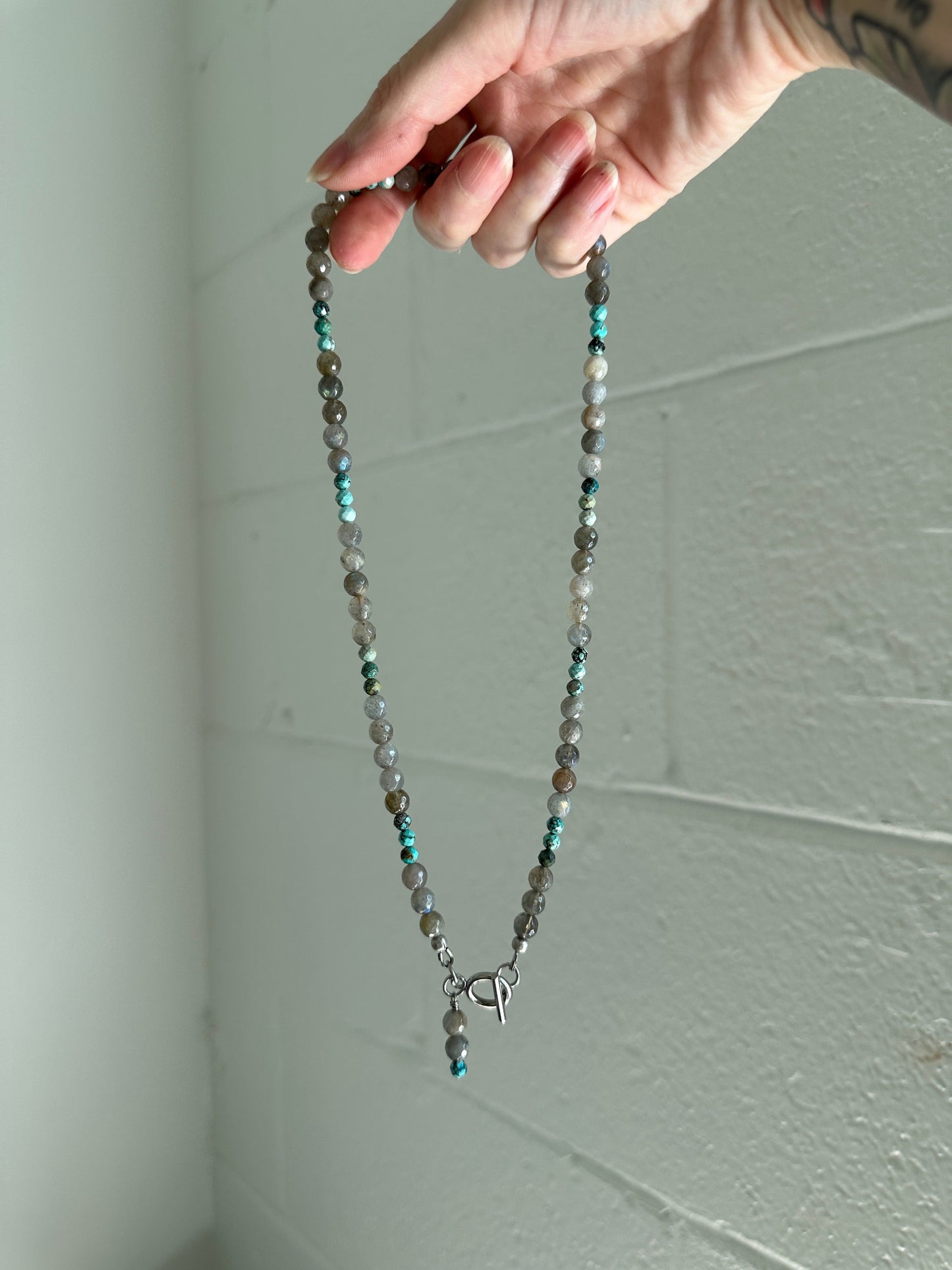 Hand holding a beaded necklace against a white ceiling background