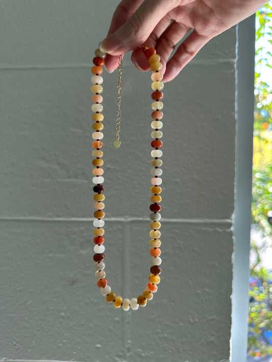 Hand holding a beaded necklace against a light gray wall